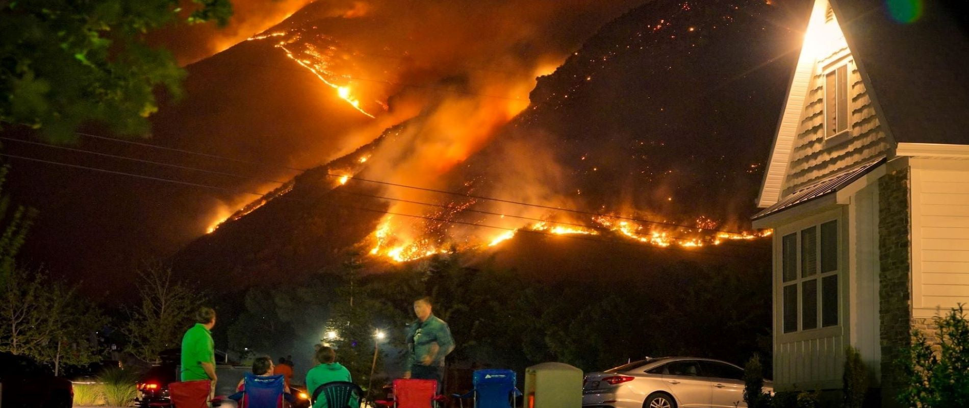 Mountainous Natural Disaster Wildfire at night approaching house, vehcles and people watching. 